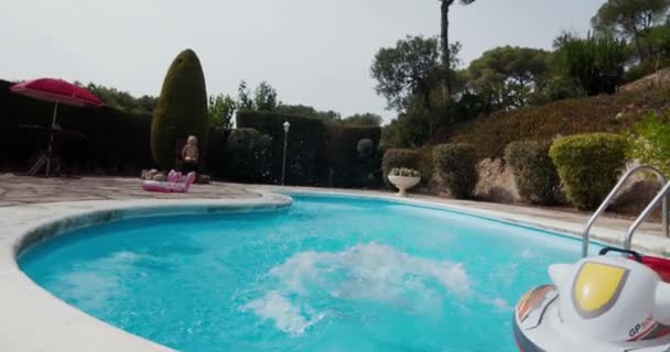 Niño vista trasera está corriendo y saltando en el agua de la piscina — Vídeo de stock