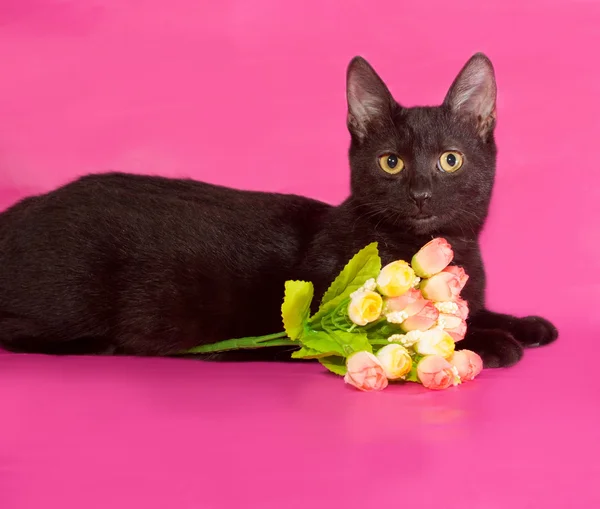 Black kitten with bouquet of flowers lying on pink — Stock Photo, Image