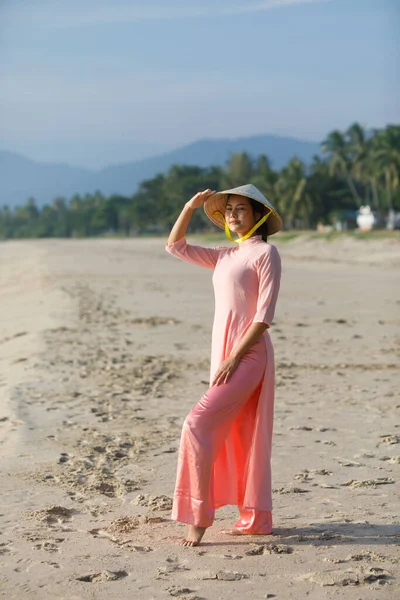 A young woman in a Vietnamese dress pose on the beach in the morning.