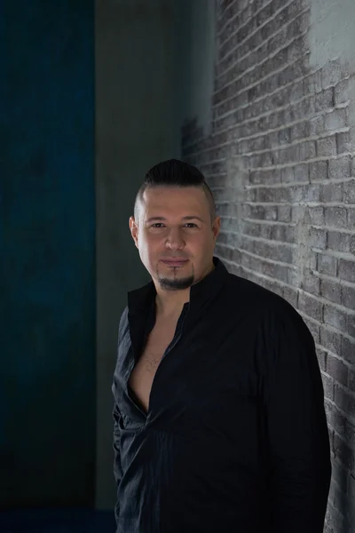 Portrait of a young man, dressed in black shirt, fashionable hairstyle with shaved temples and slicked back hair at the top of the head, Brick wall, beard, close-up portrait