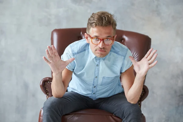 Retrato de un hombre inteligente con estilo mira a la cámara, pequeño sin afeitar, carismático, camisa azul, sentado en una silla de cuero marrón, diálogo, negociación, manga corta, brutal, peinado —  Fotos de Stock