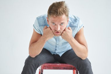 Acımasız adam kırmızı sandalye üzerinde yumruklarını sıktı, oturan kısa kollu gömlekli hafifçe, diz, dalgın eğildi alın, bakışları altında eğildi