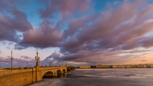 Rusia, San Petersburgo, 19 de marzo de 2016: Nubes rosadas sobre el puente Troitsky al atardecer, hielo a la deriva, río Neva congelado, el tráfico en el puente, un paseo peatonal, Troitskiy — Foto de Stock