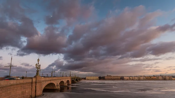 Rusia, San Petersburgo, 19 de marzo de 2016: Nubes rosadas sobre el puente Troitsky al atardecer, hielo a la deriva, río Neva congelado, el tráfico en el puente, un paseo peatonal, Troitskiy — Foto de Stock