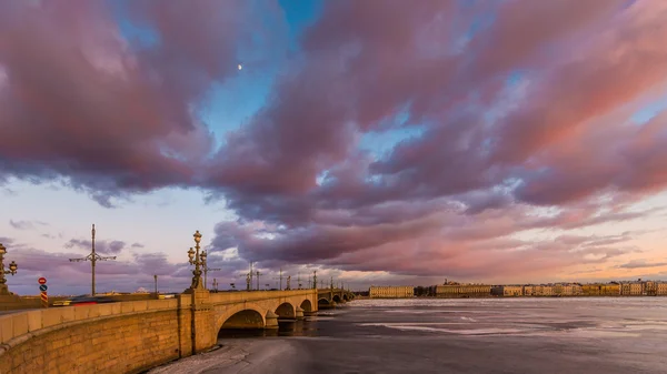 Rusia, San Petersburgo, 19 de marzo de 2016: Nubes rosadas sobre el puente Troitsky al atardecer, hielo a la deriva, río Neva congelado, el tráfico en el puente, un paseo peatonal, Troitskiy — Foto de Stock