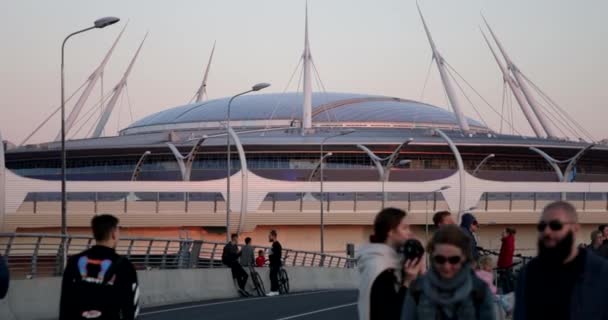 Rússia, São Petersburgo, 01 de setembro de 2020: As pessoas estão andando na ponte ao pôr do sol durante a pandemia de covid-19, andar de eletroskate, estão fazendo o quadro, a arena Gazprom está no fundo — Vídeo de Stock