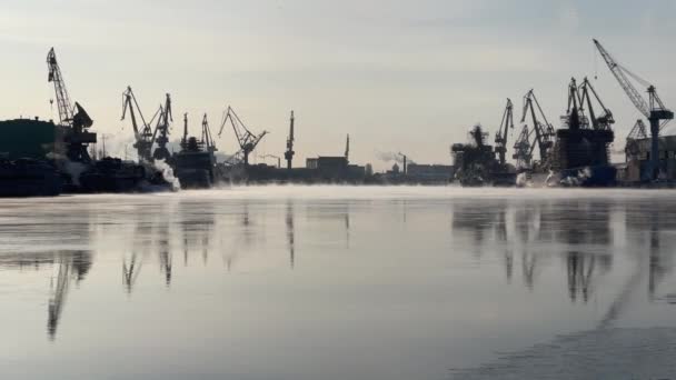 Краны Балтийской верфи в морозный зимний день, пар над Невой, гладкая поверхность реки, зеркальное отражение на воде, строящиеся корабли, траулеры, атомные ледоколы — стоковое видео