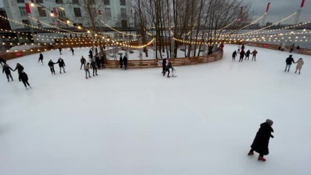 Russia, San Pietroburgo, 28 gennaio 2021: pista di pattinaggio nel territorio dell'ex impianto, ghirlande su una pista di pattinaggio, tempo cupo, giochi musicali, famiglie con bambini e coppie felici — Video Stock