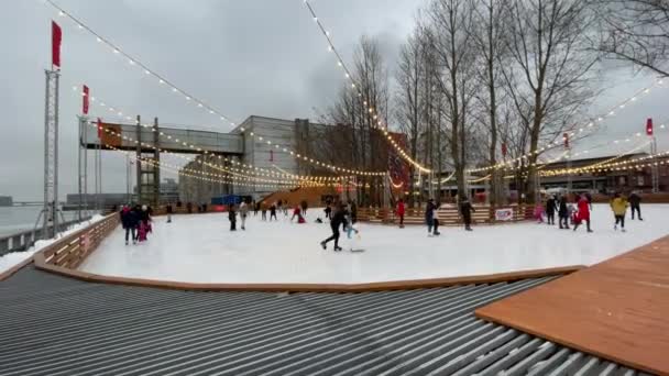 Rusia, San Petersburgo, 28 de enero de 2021: pista de patinaje en el territorio de la antigua planta, guirnaldas sobre una pista de patinaje, tiempo sombrío, obras de música, familias con niños y parejas felices — Vídeo de stock