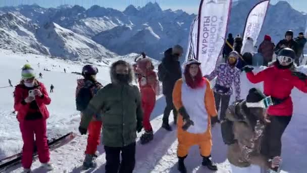 Oroszország, Kabardino-Balkariya, 2021. január 07.: A DJ az Elbrus-hegy legnépszerűbb pontján játszik, a snowboardosok táncolnak, a hegy a háttérben, Azaus síközpont — Stock videók
