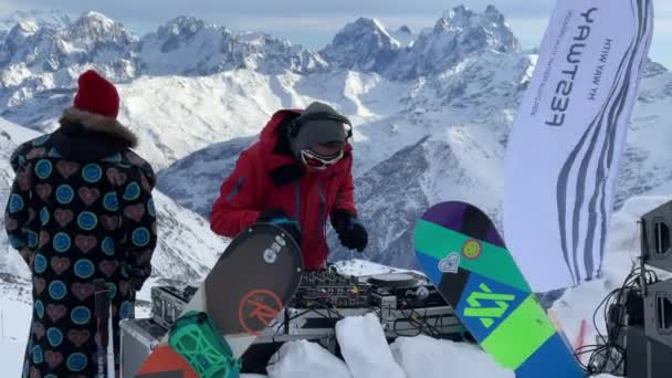 Oroszország, Kabardino-Balkariya, 2021. január 07.: A DJ az Elbrus-hegy legnépszerűbb pontján játszik, a lány a közelben táncol, a hegy a háttérben, Azaus síközpont — Stock videók