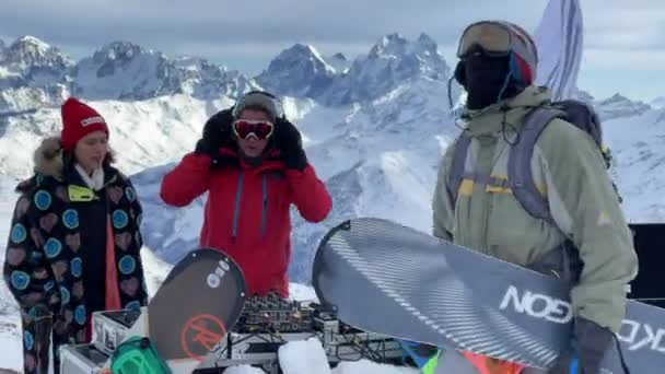 Rosja, Kabardino-Balkariya, 07 stycznia 2021 r.: DJ gra na szczycie góry Elbrus, dziewczyna tańczy w pobliżu, snowboardzista tańczy, góra na tle, ośrodek narciarski Azaus — Wideo stockowe
