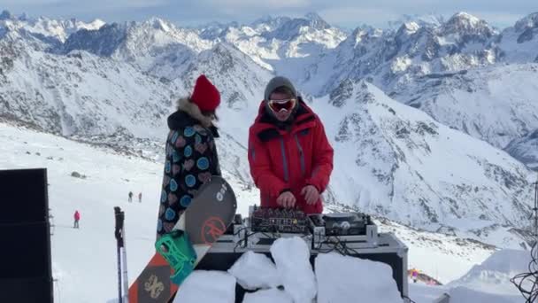 Россия, Кабардино-Балкария, 07 января 2021: DJ играет на самой высокой отметке Эльбруса, девушка танцует неподалеку, гора на заднем плане, горнолыжный курорт Азаус — стоковое видео