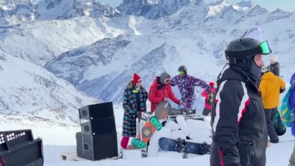 Oroszország, Kabardino-Balkariya, 2021. január 07.: A DJ az Elbrus-hegy legnépszerűbb pontján játszik, a snowboardosok táncolnak, a hegy a háttérben, Azaus síközpont — Stock videók