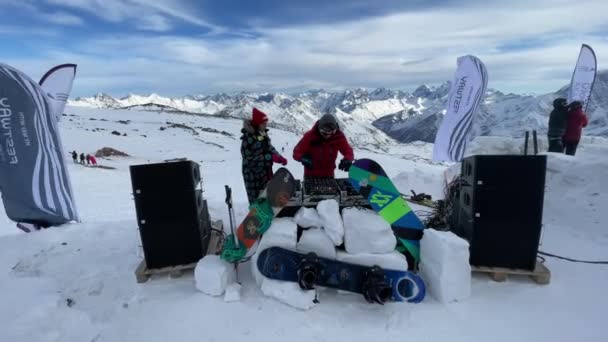 Rusia, Kabardino-Balkariya, 07 Enero 2021: El DJ juega en la marca más alta del Monte Elbrus, la chica baila cerca, la montaña en un fondo, Azaus estación de esquí — Vídeo de stock