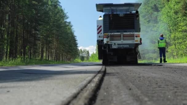 Росія, Санкт-Петербург, 28 червня 2019: Освоєння нового асфальту, спеціальні автомобілі, ковзанка, дорога в лісі, ліси, зелені дерева, сонячний день, робітники, стеки нового асфальту — стокове відео