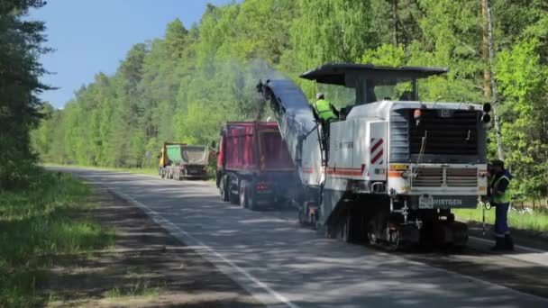 Росія, Санкт-Петербург, 28 червня 2019: Освоєння нового асфальту, спеціальні автомобілі, ковзанка, дорога в лісі, ліси, зелені дерева, сонячний день, робітники, стеки нового асфальту — стокове відео