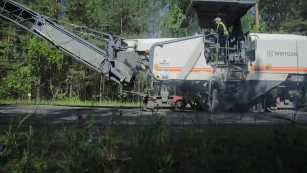 Russia, St.Petersburg, 28 June 2019: Laying of the new asphalt, special cars, skating rink, the road in the wood, forest, green trees, sunny day, workers, the car stacks new asphalt — Stock Video