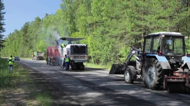 Ryssland, St Petersburg, 28 juni 2019: Lägger ny asfalt, specialbilar, skridskobana, vägen i skogen, skog, gröna träd, solig dag, arbetare, bilen staplar ny asfalt — Stockvideo