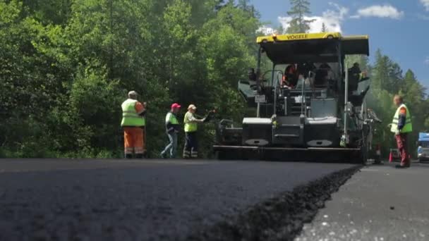 Russia, San Pietroburgo, 28 giugno 2019: Posa del nuovo asfalto, auto speciali, pista di pattinaggio, la strada nel bosco, foresta, alberi verdi, giornata di sole, lavoratori, l'auto impila nuovo asfalto — Video Stock