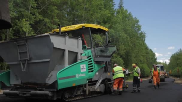 Ρωσία, Αγία Πετρούπολη, 28 Ιουνίου 2019: Τοποθέτηση νέας ασφάλτου, ειδικών αυτοκινήτων, παγοδρόμιο, δρόμος στο δάσος, δάσος, πράσινα δέντρα, ηλιόλουστη μέρα, εργαζόμενοι, το αυτοκίνητο στοιβάζει νέα άσφαλτο — Αρχείο Βίντεο