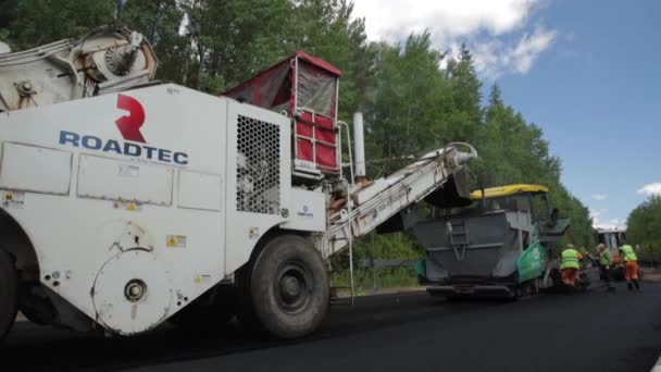 Rusia, San Petersburgo, 28 de junio de 2019: Colocación del nuevo asfalto, coches especiales, pista de patinaje, el camino en el bosque, el bosque, los árboles verdes, el día soleado, los trabajadores, el coche apila nuevo asfalto — Vídeos de Stock