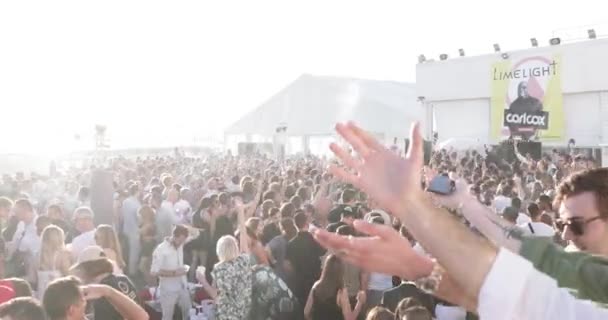 Frankrig, Cannes, 19. maj 2017: festen på en strand med mange mennesker, DJ 'en faderen til en techno Carl Cox spiller på 4 pladespillere, hænder op, solnedgang, hav og bjerge på baggrund – Stock-video