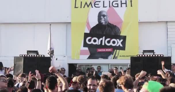 Frankrike, Cannes, 19. mai 2017: Festen på en strand med mange mennesker, DJ-en faren til en tekno, Carl Cox, spiller på 4 plateskiver, hender opp, solnedgang, hav og fjell på bakgrunn av dette – stockvideo