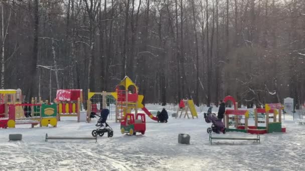Rusia, San Petersburgo, 08 Marzo 2021: Parque infantil en el parque en la tarde clara de invierno, los padres juegan con los niños, está nevando, estructuras de color brillante, árboles grises sobre un fondo — Vídeos de Stock