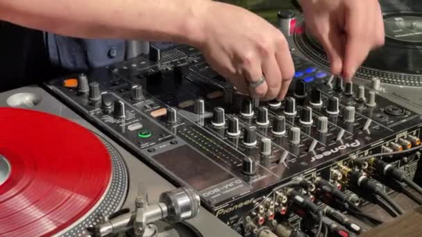 Rusko, Petrohrad, 10. března 2021: Detailní video rukou DJ za prací, vinylové desky, mixážní panel, muž, kterého DJ hraje ve studiu, stěna zelené barvy, otočí kliky na panelu — Stock video