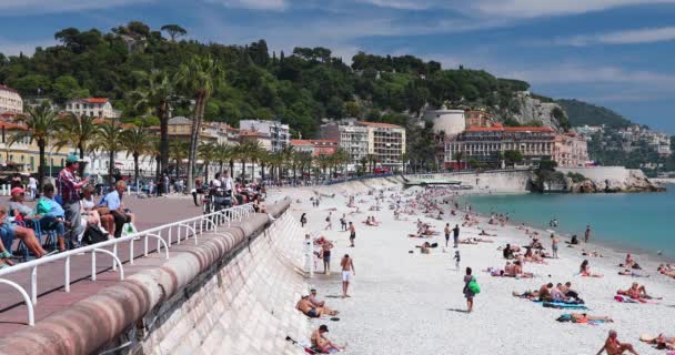 Francia, Niza, 15 de mayo de 2017: Paseo marítimo Anglais, Hermosa playa pública, Turistas, Sunbath People, Natación, Día soleado, La gente se sienta en las conocidas sillas azules, Ultra Alta Definición, UltraHD, 4K — Vídeos de Stock