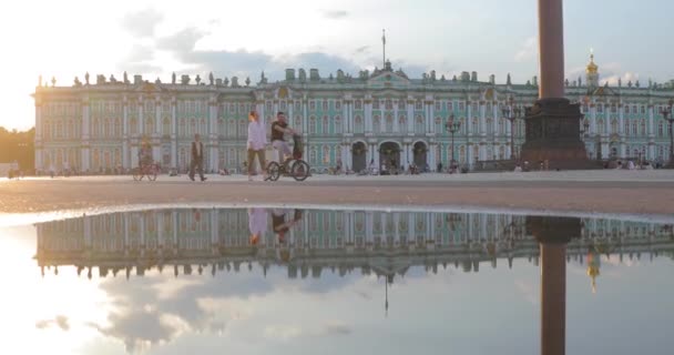 Russia, San Pietroburgo, 09 giugno 2020: Spettacolare riflessione del Palazzo d'Inverno in una piscina dopo una pioggia, i residenti attraversano Piazza del Palazzo al tramonto, la colonna di Alessandria su uno sfondo — Video Stock