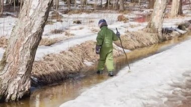Sopalı çocuk vahşi parktaki bahar su birikintisine gider. İlk bahar günlerinde yeşil tulum giyer.