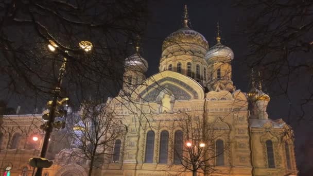 Iglesia ortodoxa de la Asunción de la Santísima Virgen en la isla Vasilyevsky de San Petersburgo, Rusia, una granja del desierto de Kozelsk San Vvedenskoy Optinoy, Lampposts, está nevando — Vídeos de Stock