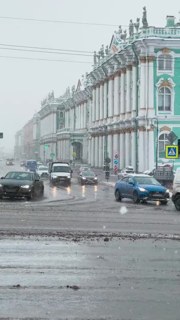 Rússia, São Petersburgo, 03 de fevereiro de 2021: Filmagem vertical do tráfego de automóveis no aterro do palácio no museu o Hermitage ou o Palácio de Inverno em dia nublado de inverno, sujeira nas estradas, nevando — Vídeo de Stock