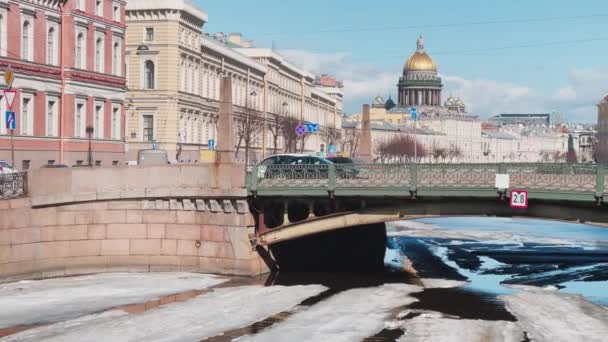 Rusia, San Petersburgo, 01 de abril de 2021: Pintoresco paisaje de una deriva de hielo en el río Moyka a través del puente de los Besos en un claro día soleado, una cúpula de oro de la Catedral de San Isaacs sobre un fondo — Vídeos de Stock