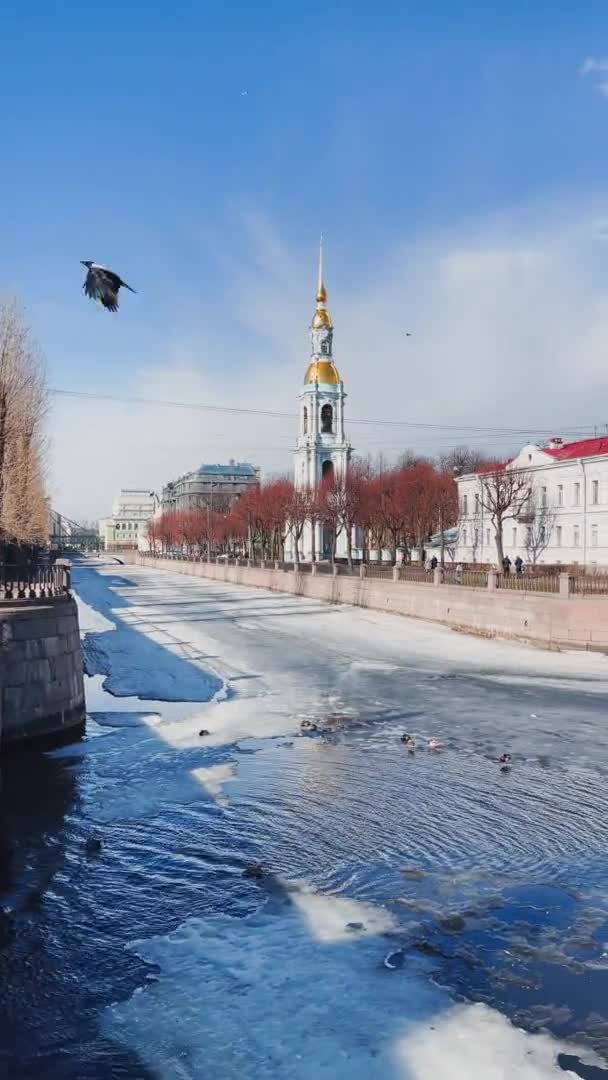 Russia, St. Petersburg, 01 April 2021: St. Nicholas Naval Cathedral belltower in a clear sunny day of spring, an ice drift on Kryukov and Griboyedov Canal, a view of seven bridges from the embankment — Stock Video