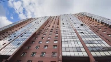 Üst kattaki balkonlu evin ön cephesi, alttaki manzara, video kameranın yavaş hareketi, tuğla rengi, bulutlu hava, büyük bir konut alanı. 