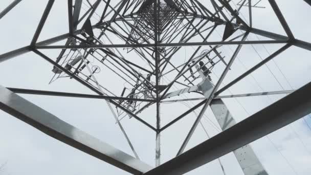 Enorme torre de metal de alto voltaje con cables eléctricos, la vista inferior hacia arriba, movimiento lento de una cámara de vídeo, tiempo nublado — Vídeos de Stock
