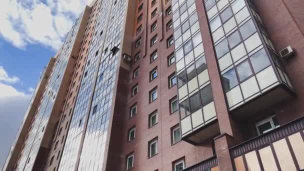 Facade of the high-floor house with the glazed balconies, the bottom view up, slow movement of a video camera, brick color, cloudy weather, a huge housing estate — Stock Video