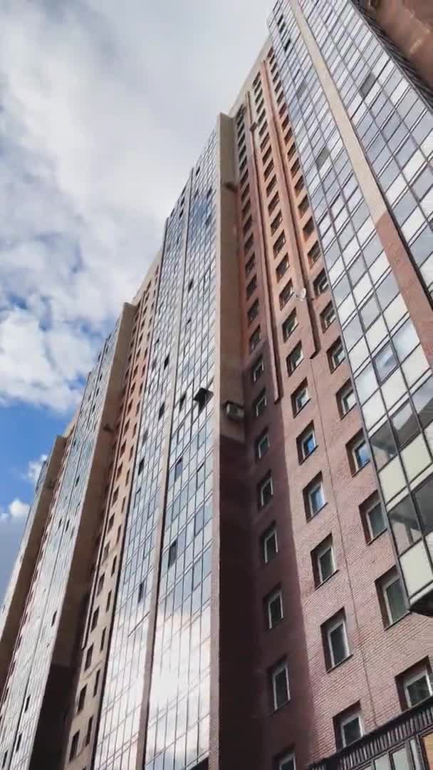 Facade of the high-floor house with the glazed balconies, the bottom view up, slow movement of a video camera, brick color, cloudy weather, a huge housing estate — стоковое видео