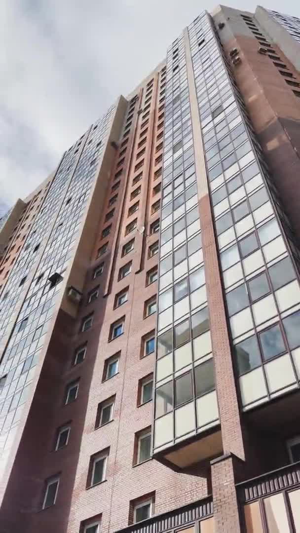 Facade of the high-floor house with the glazed balconies, the bottom view up, slow movement of a video camera, brick color, cloudy weather, a huge housing estate — стоковое видео