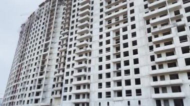 Üst kattaki evin inşaatı, inşaat vinçleri, alttaki görüntü, video kameranın yavaş hareketi, penceresiz beton bloklar ve cephe sonu, bulutlu hava, büyük bir emlak.