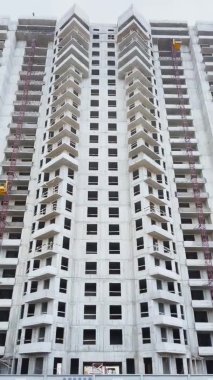 Üst kattaki evin inşaatı, inşaat vinçleri, alttaki görüntü, video kameranın yavaş hareketi, penceresiz beton bloklar ve cephe sonu, bulutlu hava, büyük bir emlak.