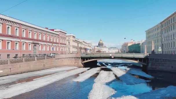 Rusya, St.Petersburg, 01 Nisan 2021: Moyka Nehri üzerinde açık güneşli bir günde Kisses Köprüsü 'nden geçen bir buz tabakasının manzarası, arka planda St. Isaacs Katedrali' nin altın kubbesi — Stok video