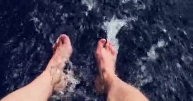 Çıplak ayaklar güneşli bir günde tekneden indirilir, yetişkin bir adamın ayakları, mavi su, sıçrama ve kabarcıklar, büyük bir hızla hareket