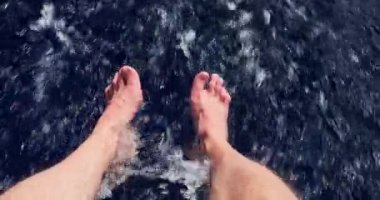 Çıplak ayaklar güneşli bir günde tekneden indirilir, yetişkin bir adamın ayakları, mavi su, sıçrama ve kabarcıklar, büyük bir hızla hareket