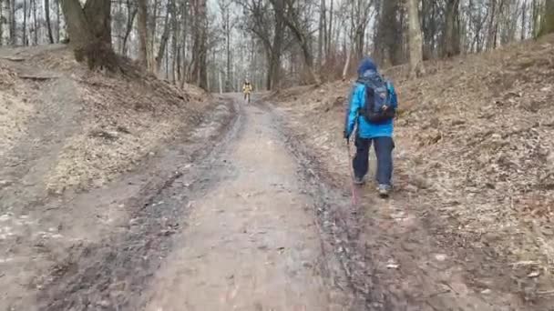 Rússia, São Petersburgo, 08 de abril de 2021: A visão traseira do viajante com paus de pé, ele se levanta em uma colina na floresta, de costas para ele a mochila pendura, A menina de bicicleta para ele em direção — Vídeo de Stock