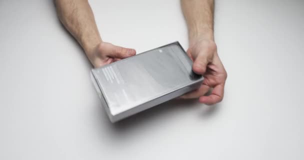 Ρωσία, Αγία Πετρούπολη, 09 Απριλίου 2021: Μια διαδικασία αποσυσκευασίας iPhone 12 Pro Max σε λευκό φόντο πίνακα, τα χέρια αφαιρώντας το πλαστικό περιτύλιγμα από το μαύρο κουτί της νέας συσκευής, χρώμα γραφίτη — Αρχείο Βίντεο
