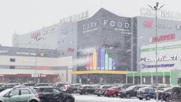 Rusland, Sint-Petersburg, 18 maart 2021: Zware sneeuwval in de stad, een parkeerplaats voor auto 's bij groot winkelcentrum, een sneeuwstorm, sneeuwstorm, sneeuwstorm, veelkleurige borden op het gebouw — Stockvideo